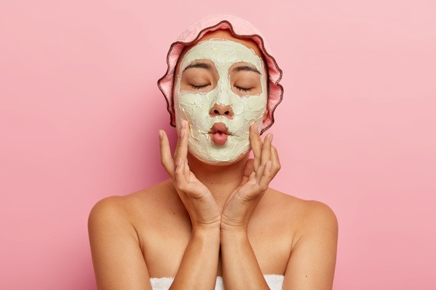Cerrar imagen mujer complacida aplica mascarilla facial casera piel seca hace boca pez tiene tratamiento spa muestra hombros desnudos usa gorro bano toalla preocupa apariencia aislado rosa 273609 27956