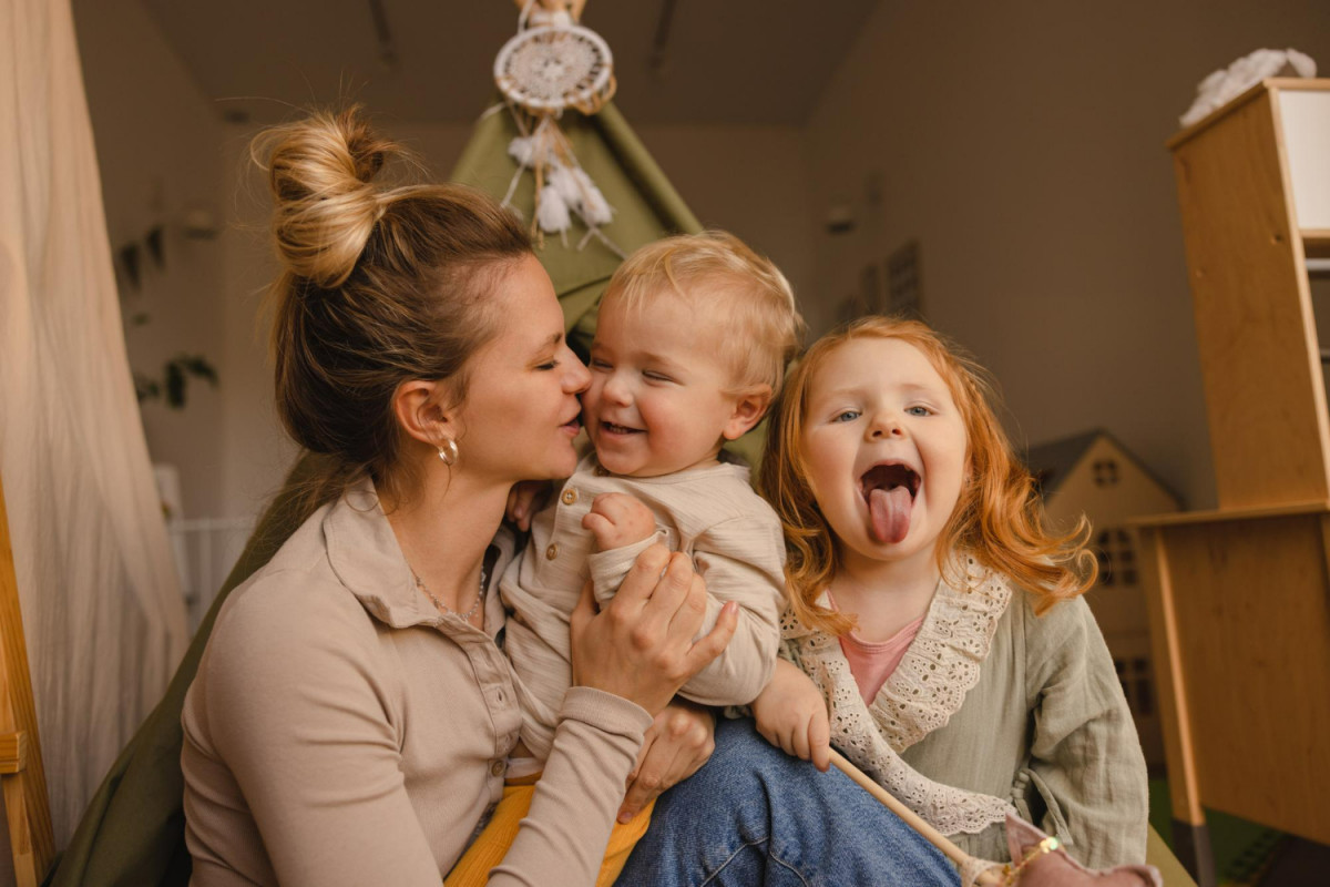 Cute young caucasian mother son and daughter hugging spending time together in room on weekend parents play with children concept